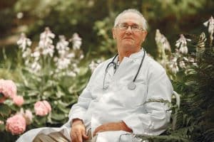 Retired elderly doctor sitting on a park bench in summer, reflecting on medical career