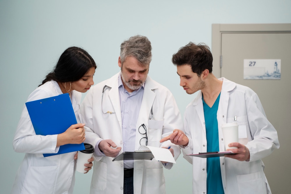 Three doctors in white coats discussing patient case in hospital