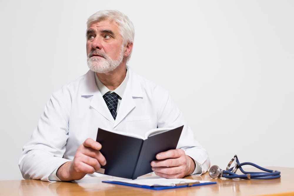 Senior doctor nearing retirement sitting on park bench in sunlight, looking contemplative