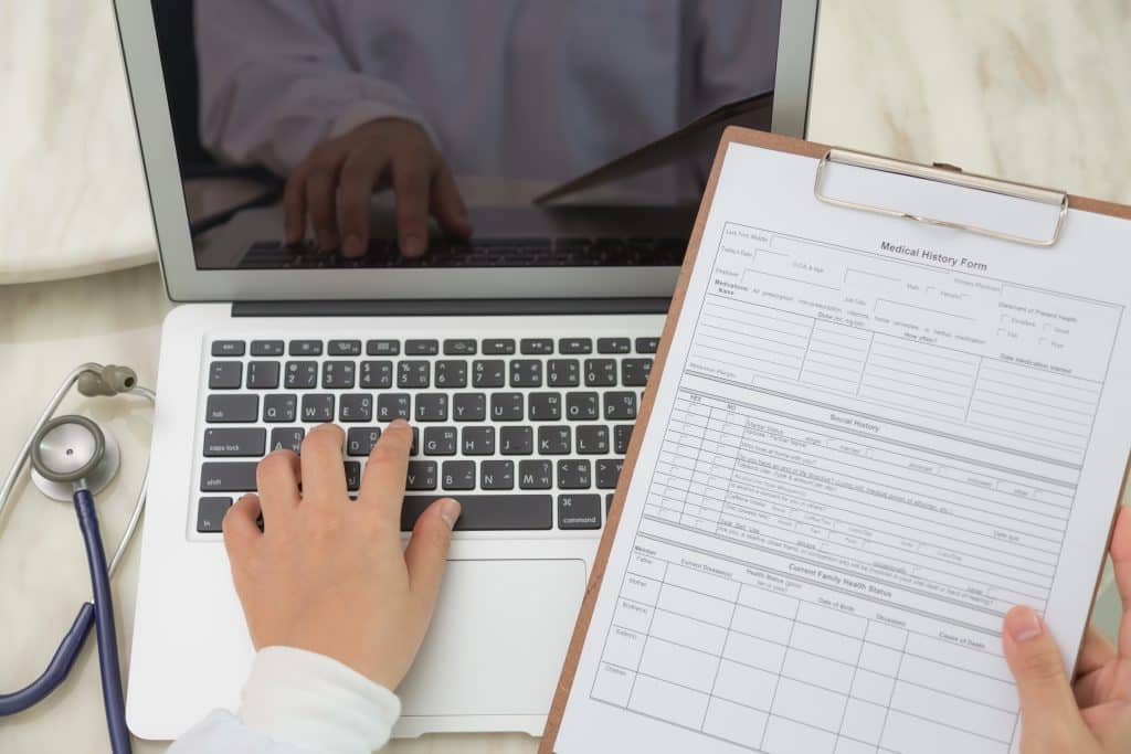 Top view of doctor working on laptop and writing on clipboard