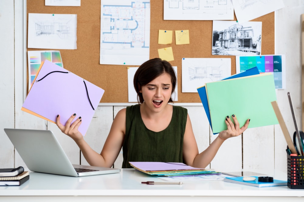 Upset young woman holding file folders in office setting, looking frustrated or stressed