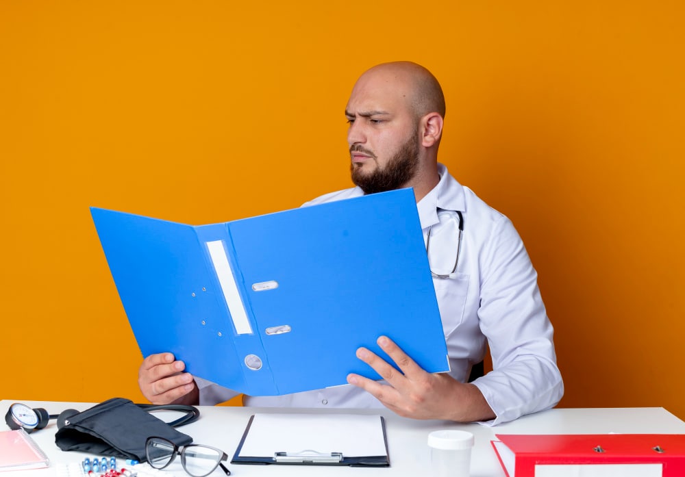 Male doctor in white coat reviewing patient medical records with stethoscope