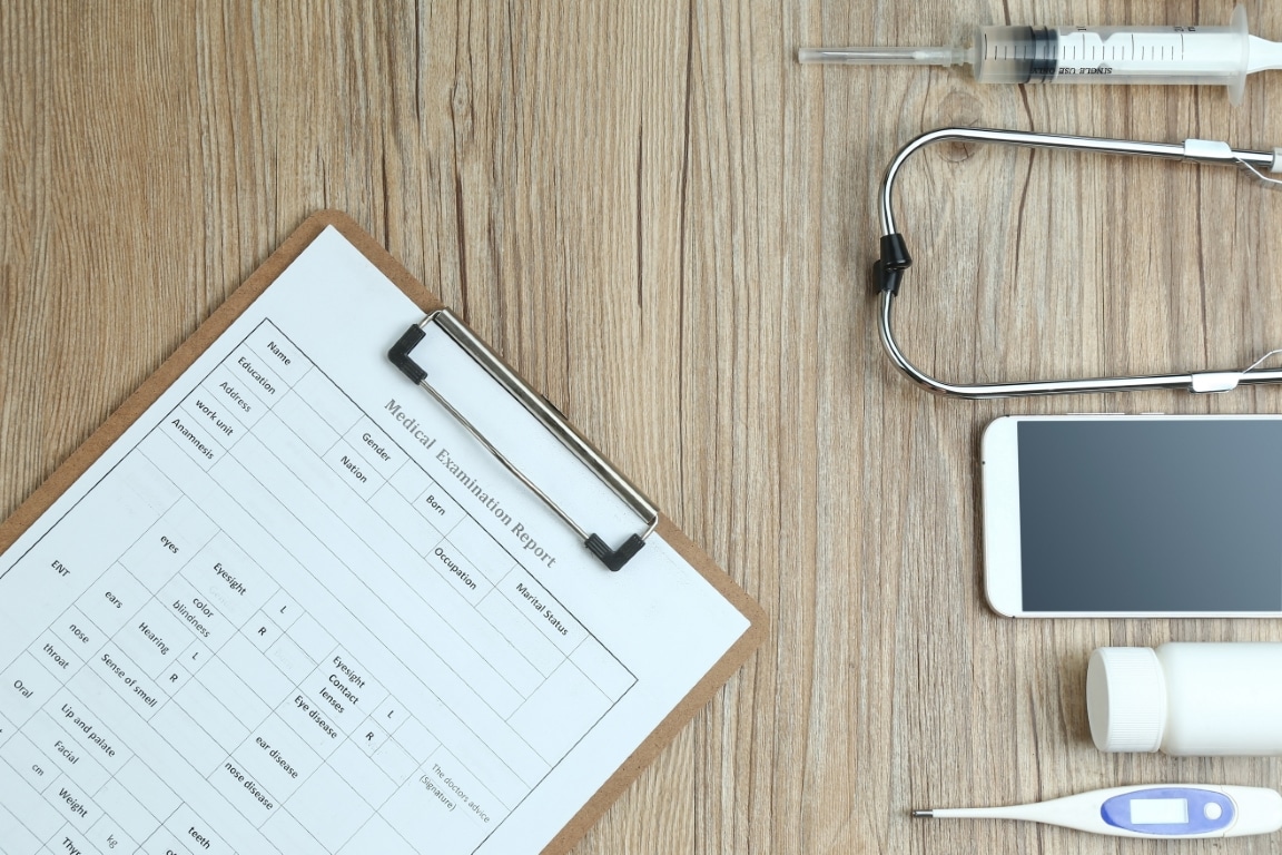 Top view of a wooden desk with medical examination report, smartphone, and clinical tools