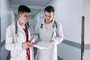 Two young doctors in white coats reviewing a patient’s medical record in a modern hospital.