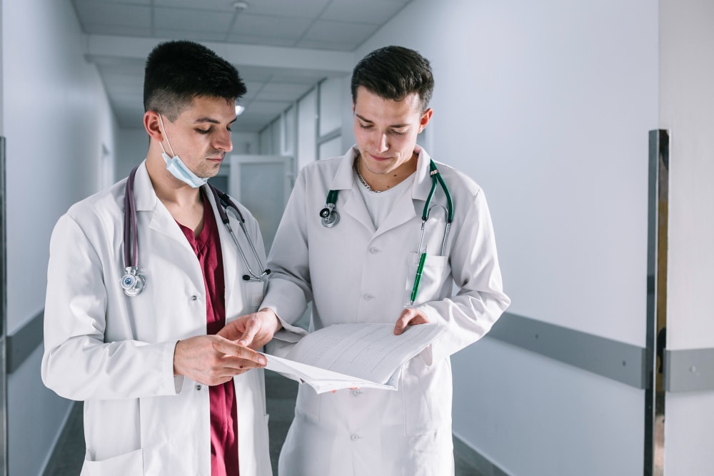 Two young doctors in white coats reviewing a patient’s medical record in a modern hospital.