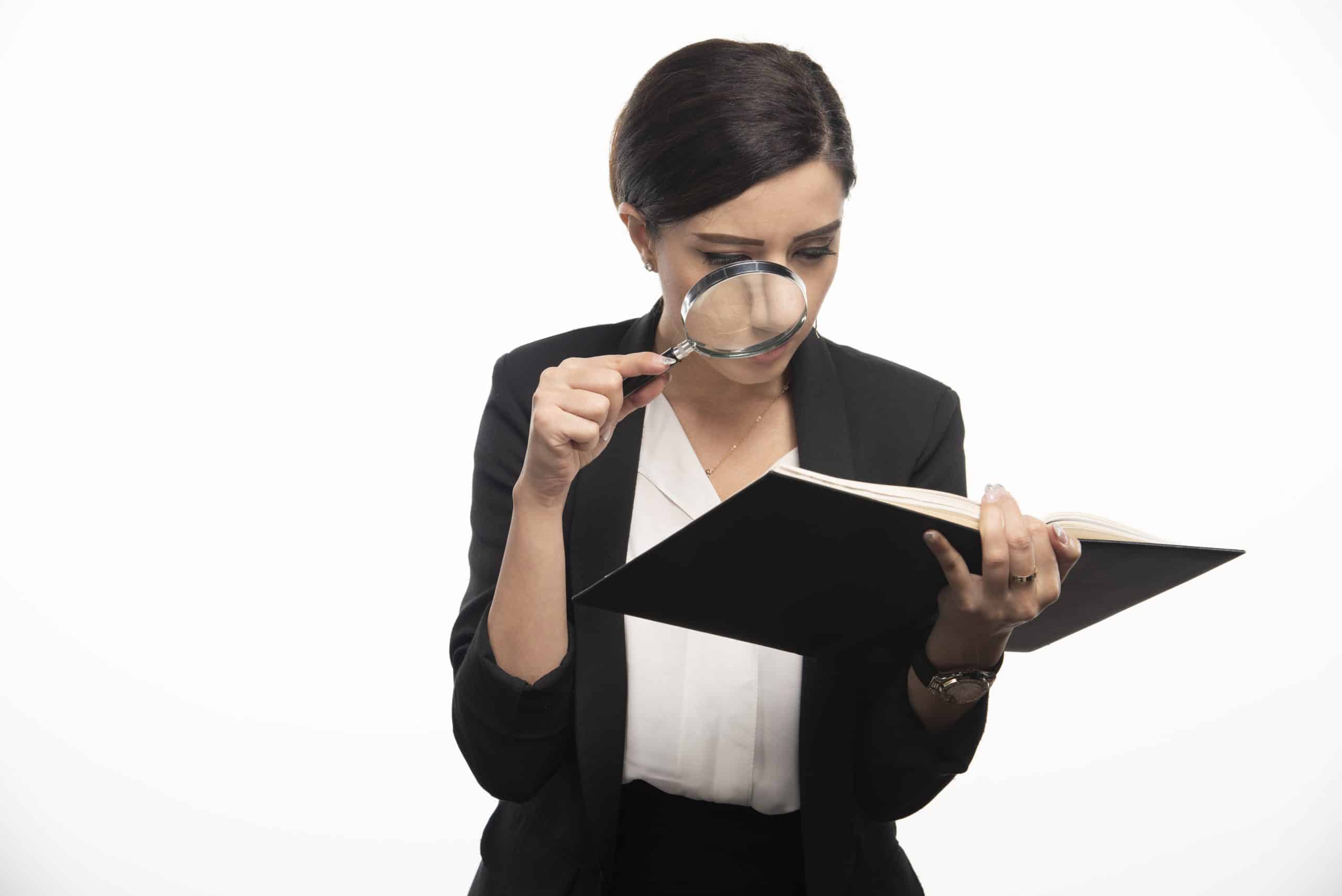 Young woman examining notebook with magnifying glass